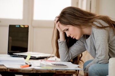 Frustrated woman looking at paperwork with a calculator and laptop on the table