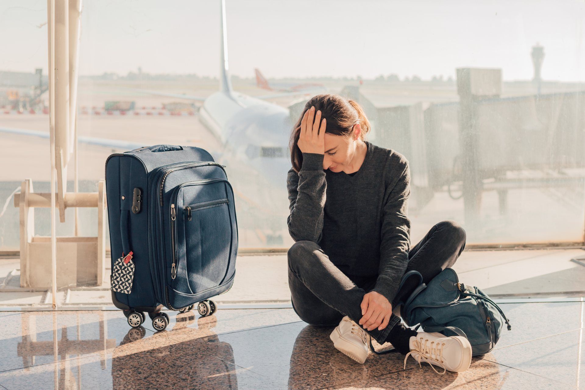 Disappointed woman sitting on floor of airport with suitcase