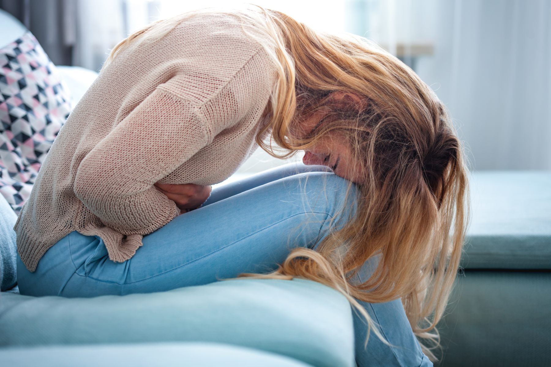 Woman sitting doubled over in pain on couch - IMMDS review of pelvic mesh shows health system failed women