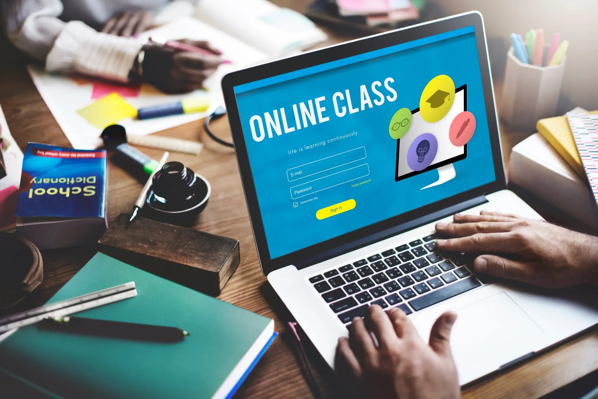 Person studying at table with "online class" screen up on laptop