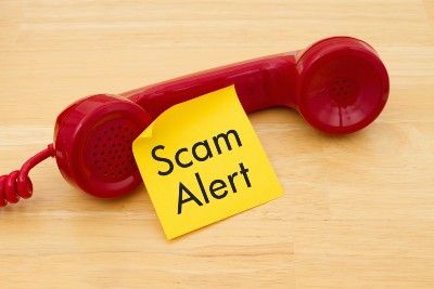 Red phone receiver with yellow sticky note that says "scam alert"