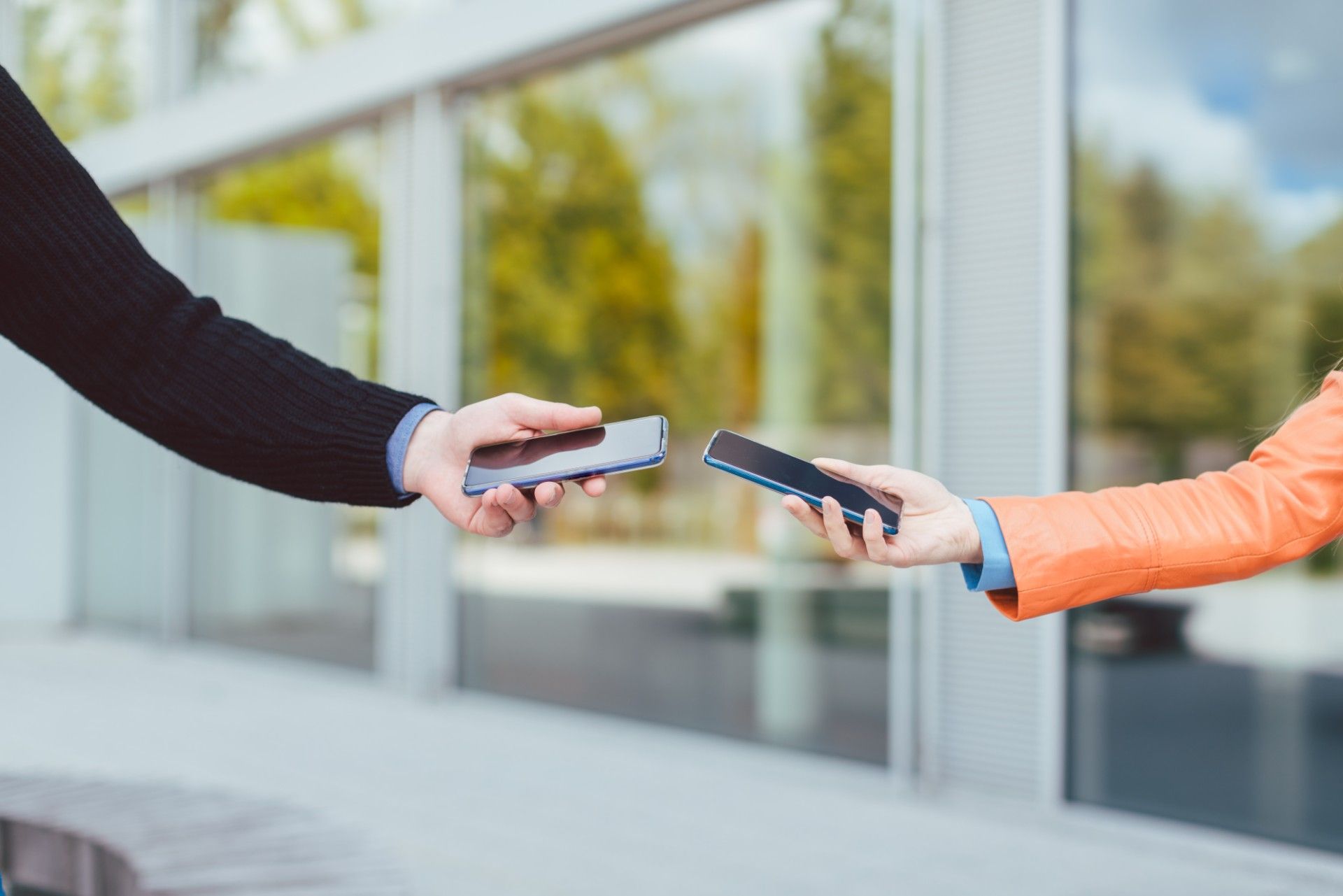 Man and woman hold smartphones near each other outside a building - contact tracing app