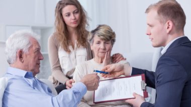 Older man signs paperwork for man in suit as family watches - assisted dying