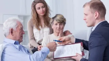 Older man signs paperwork for man in suit as family watches - assisted dying