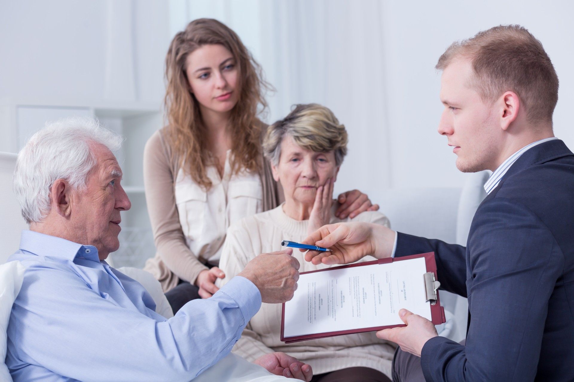 Older man signs paperwork for man in suit as family watches - assisted dying