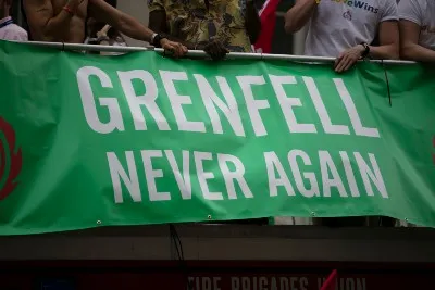 People stand near green "Grenfell Never Again" banner - cladding