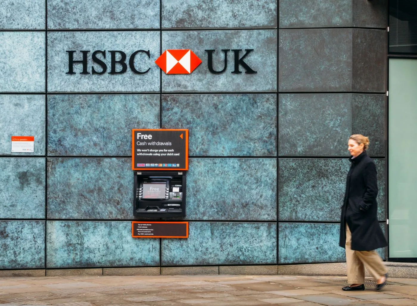 A woman walks by an HSBC UK bank cash machine in a wall - HSBC text scam