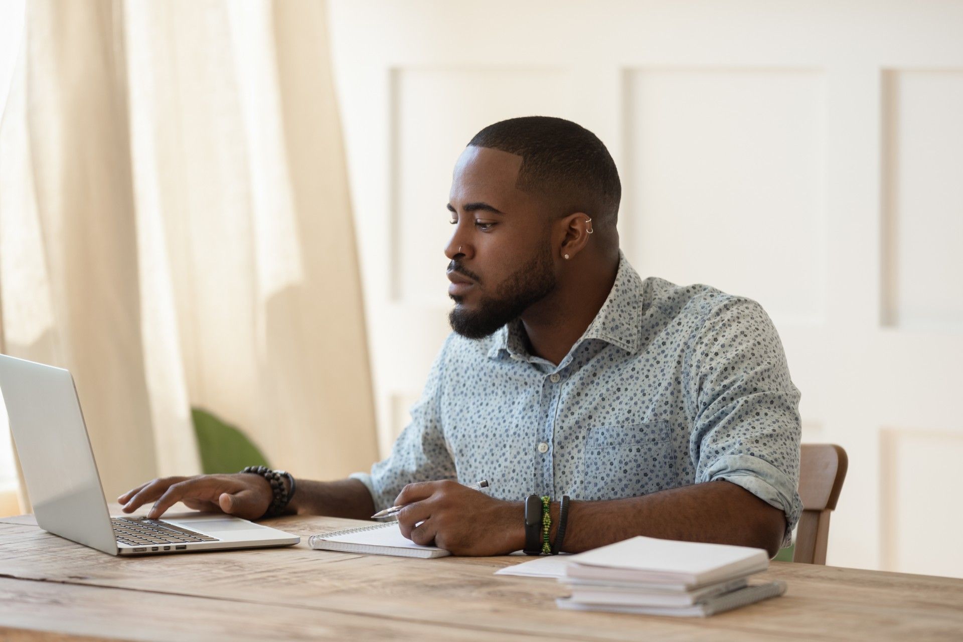 A man studies at home using a laptop and notebooks at a table - tuition fee refunds