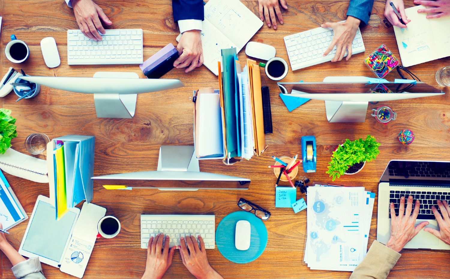 Overhead shot of four people working at busy office workstations - return to work