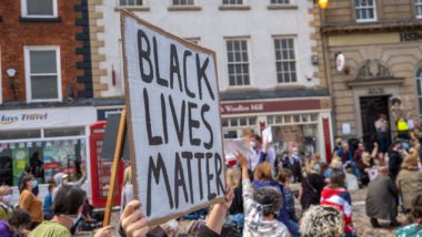 Richmond, North Yorkshire, UK - June 14, 2020: A Black Lives Matter placard is held up above a kneeling crowd at a protest in Richmond, North Yorkshire — BLM UK