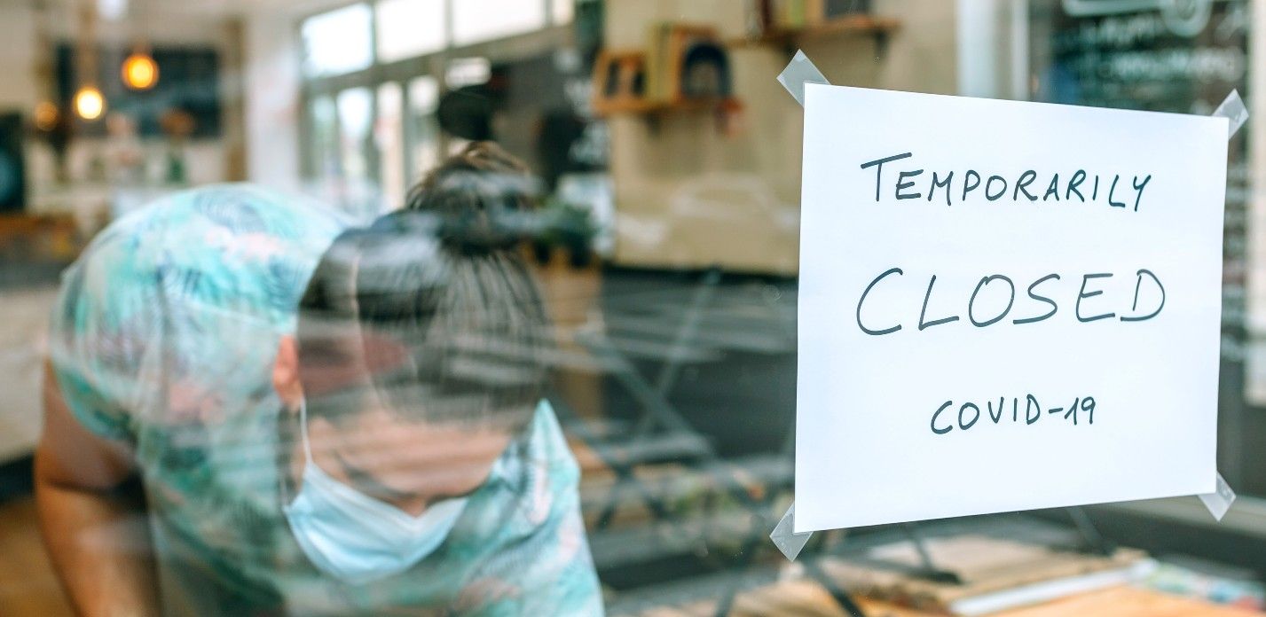 Man cleans up inside restaurant with a sign in the window that reads "temporarily closed covid-19" - lockdown legal challenge