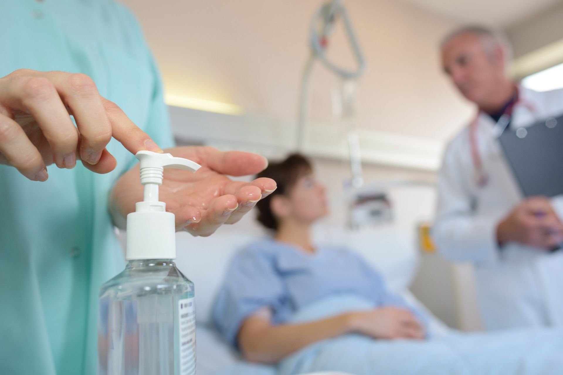 A healthcare worker pumps hand sanitiser into their hand as a doctor and patient talk in the background - virapro hand sanitiser
