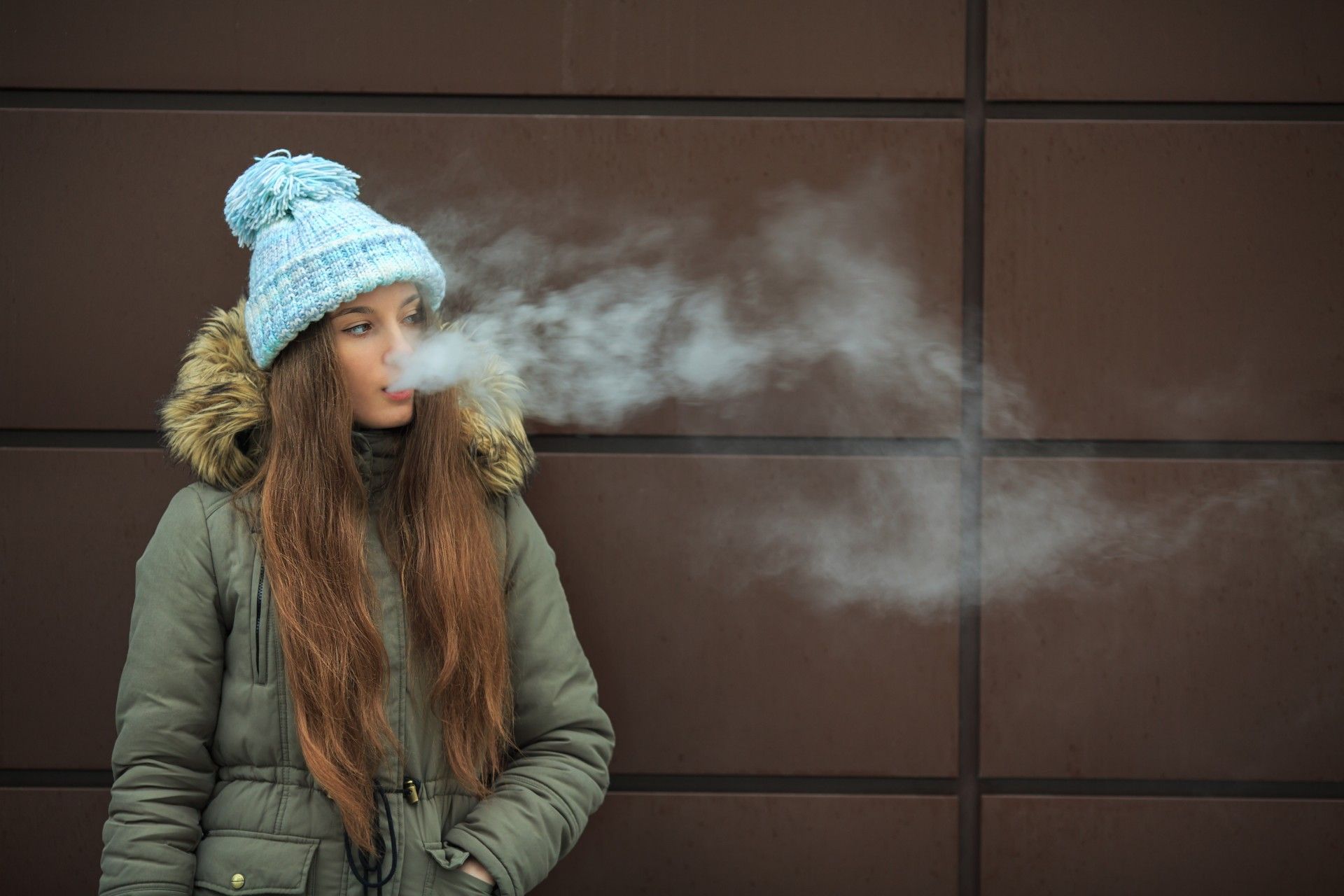 A teen girl in a coat and blue winter hat vapes - vape samples
