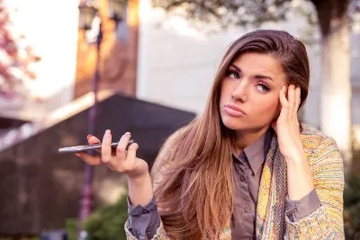 An annoyed woman holds her cellphone out like she's not listening to the caller - nuisance calls