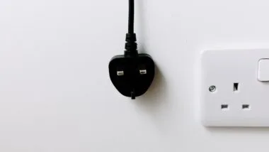 A black plug from the United Kingdom is hanging on white background. energy crisis concept.
