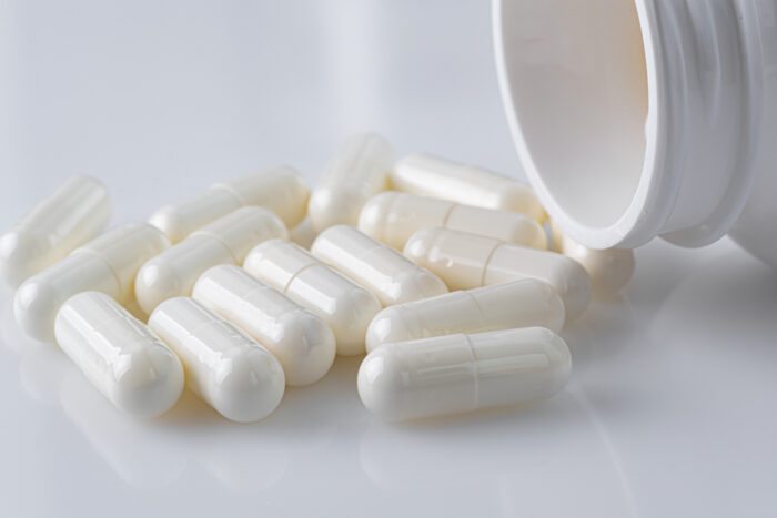 White plastic medicine vial can bottle with white capsules on white background.