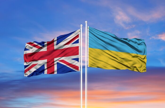 Ukraine and United Kingdom two flags on flagpoles and blue sky.
