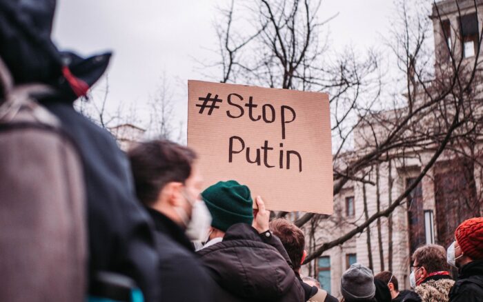 People in the streets protesting against war. A sign reads '#Stop Putin.'