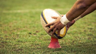 rugby player preparing to kick the oval ball during game.