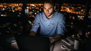A young businessman working on his laptop at night, representing the unpaid overtime survey.