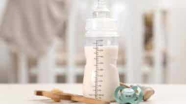 Feeding bottle with baby formula, pacifier and toys on white table indoors