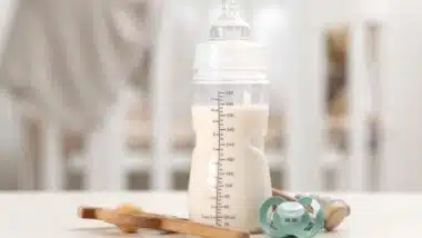 Feeding bottle with baby formula, pacifier and toys on white table indoors