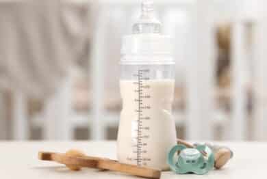 Feeding bottle with baby formula, pacifier and toys on white table indoors