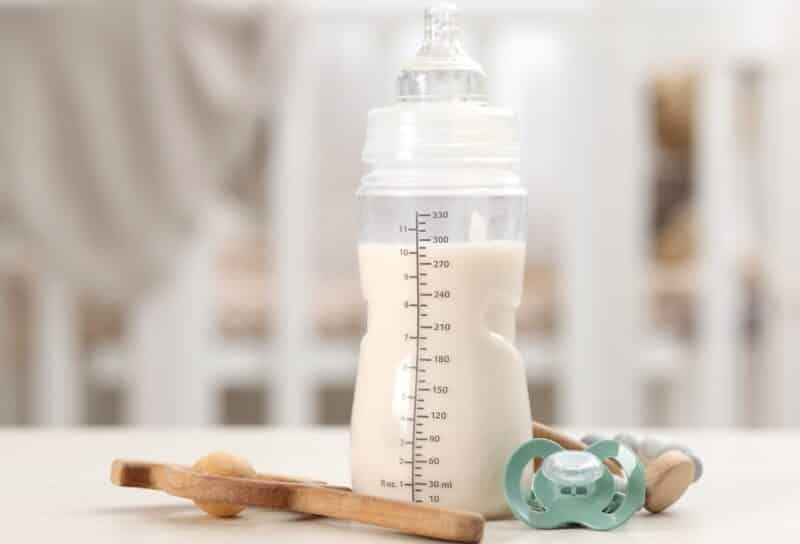 Feeding bottle with baby formula, pacifier and toys on white table indoors